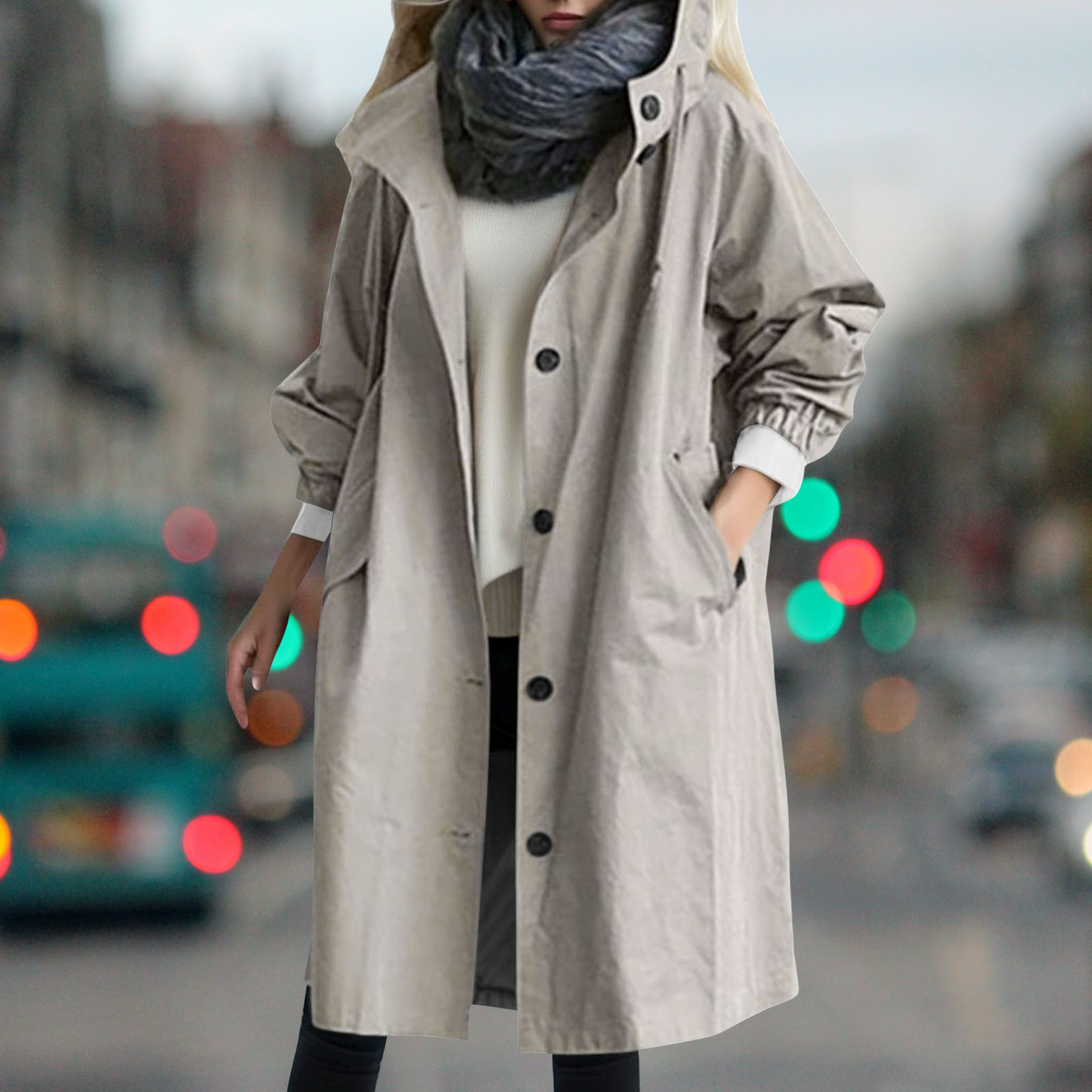 Cappotto beige donna, lungo e con bottoni, indossato su maglione bianco e sciarpa grigia, sfondo urbano sfocato, moda autunnale elegante.