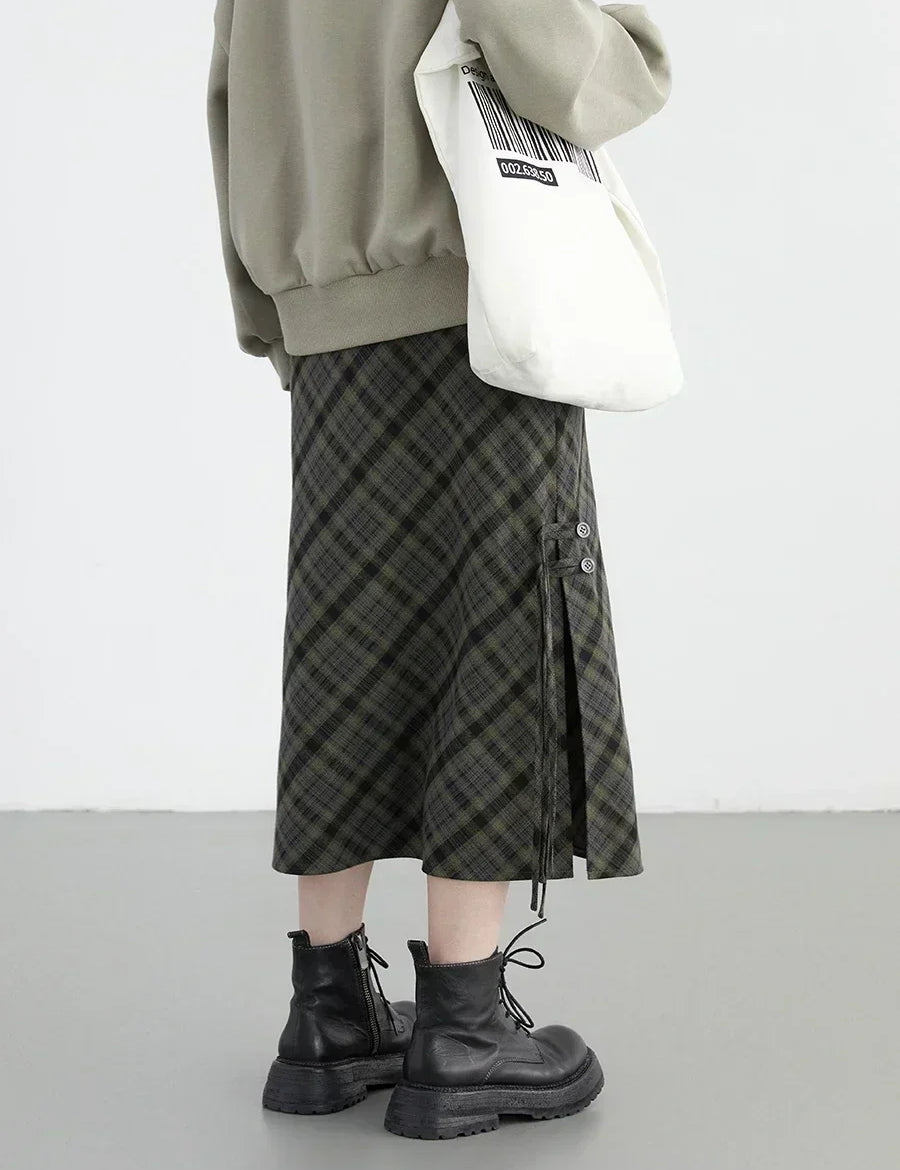 Gonna a quadri verde e nera, lunghezza media, abbinata a stivali neri e borsa bianca con codice a barre. Moda casual autunnale donna.