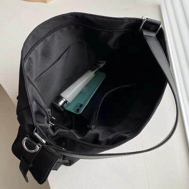 Borsa a tracolla nera aperta con tasca interna, contenente una bottiglia d'acqua e uno smartphone verde. Design elegante e spazioso.