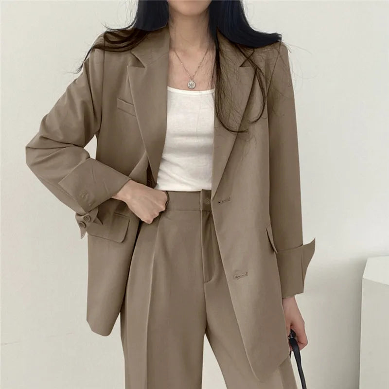 Donna in abito elegante beige, giacca e pantaloni coordinati, indossa top bianco. Moda femminile, abbigliamento formale, stile business casual.