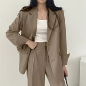 Donna in abito elegante beige, giacca e pantaloni coordinati, indossa top bianco. Moda femminile, abbigliamento formale, stile business casual.