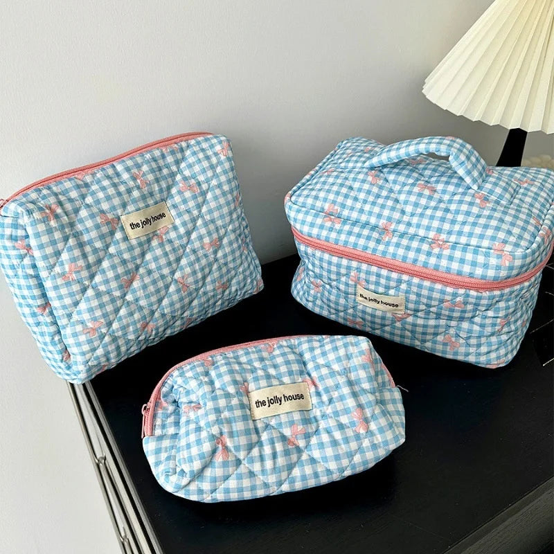 Set di tre beauty case trapuntati a quadretti azzurri con dettagli rosa, ideali per organizzare cosmetici e accessori da viaggio.
