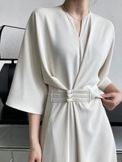 Abito bianco elegante con maniche ampie e cintura decorativa, indossato da una donna. Perfetto per cerimonie e occasioni formali.