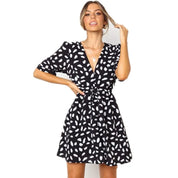 Abito corto nero a pois bianchi, maniche corte, scollo a V, donna sorridente. Moda femminile elegante, abbigliamento estivo casual.