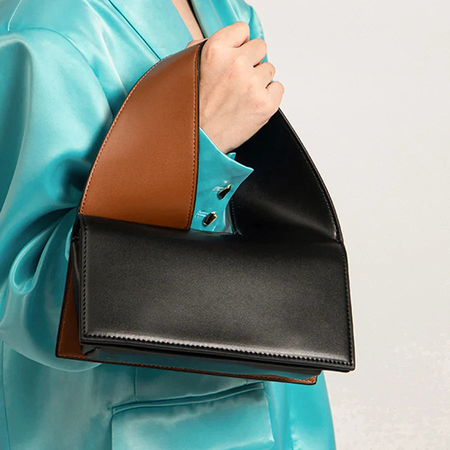 Borsa a mano in pelle nera e marrone, design moderno, indossata con giacca turchese. Accessorio moda elegante e di tendenza.