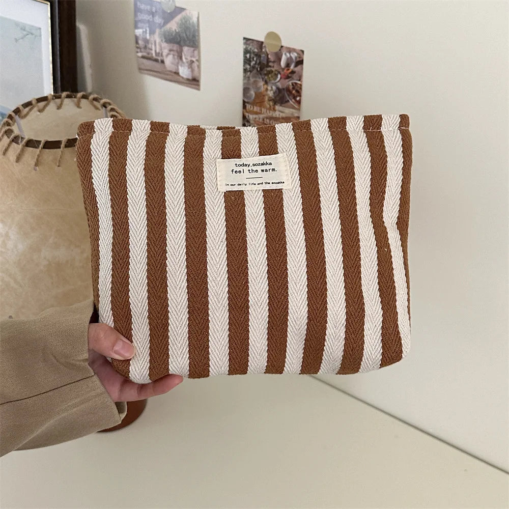 Pochette a righe marroni e bianche in tessuto, con etichetta frontale. Design elegante e moderno, ideale per accessori moda.