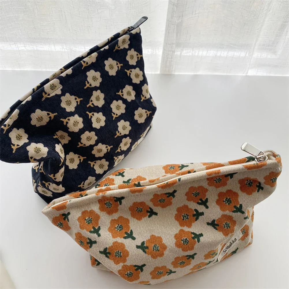 Due astucci in tessuto floreale, uno blu con fiori bianchi e uno beige con fiori arancioni, su sfondo bianco. Accessori moda eleganti e pratici.