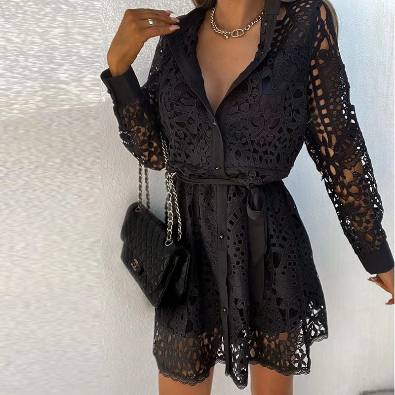 Abito corto in pizzo nero elegante, maniche lunghe, cintura in vita, borsa a tracolla nera, look da sera chic e sofisticato.