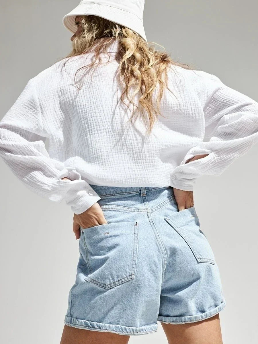 Donna con camicia bianca e shorts di jeans chiari, cappello a secchiello. Moda casual estiva, abbigliamento femminile trendy.