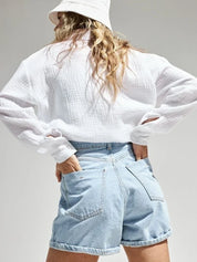 Donna con camicia bianca e shorts di jeans chiari, cappello a secchiello. Moda casual estiva, abbigliamento femminile trendy.