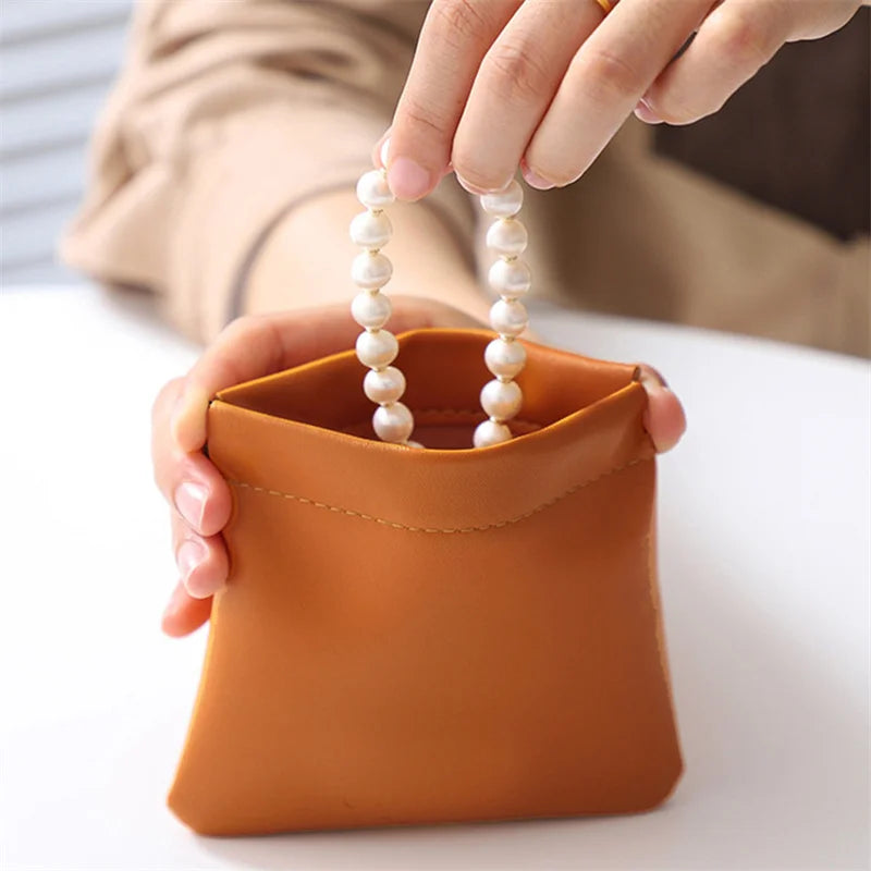 Mano che estrae collana di perle da borsa in pelle marrone. Accessori moda, gioielli eleganti, design minimalista. Perfetto per regali di lusso.