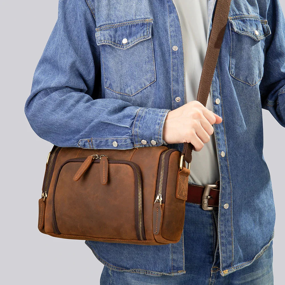 Borsa a tracolla in pelle marrone, indossata da una persona con camicia di jeans. Design elegante, ideale per uomo, moda casual.