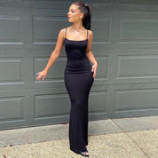 Donna con abito lungo nero aderente davanti a un garage grigio. Moda elegante, abbigliamento serale, stile sofisticato.