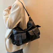 Borsa a tracolla nera in pelle con tasche multiple, indossata su giacca beige. Design elegante e funzionale, ideale per moda urbana e casual.