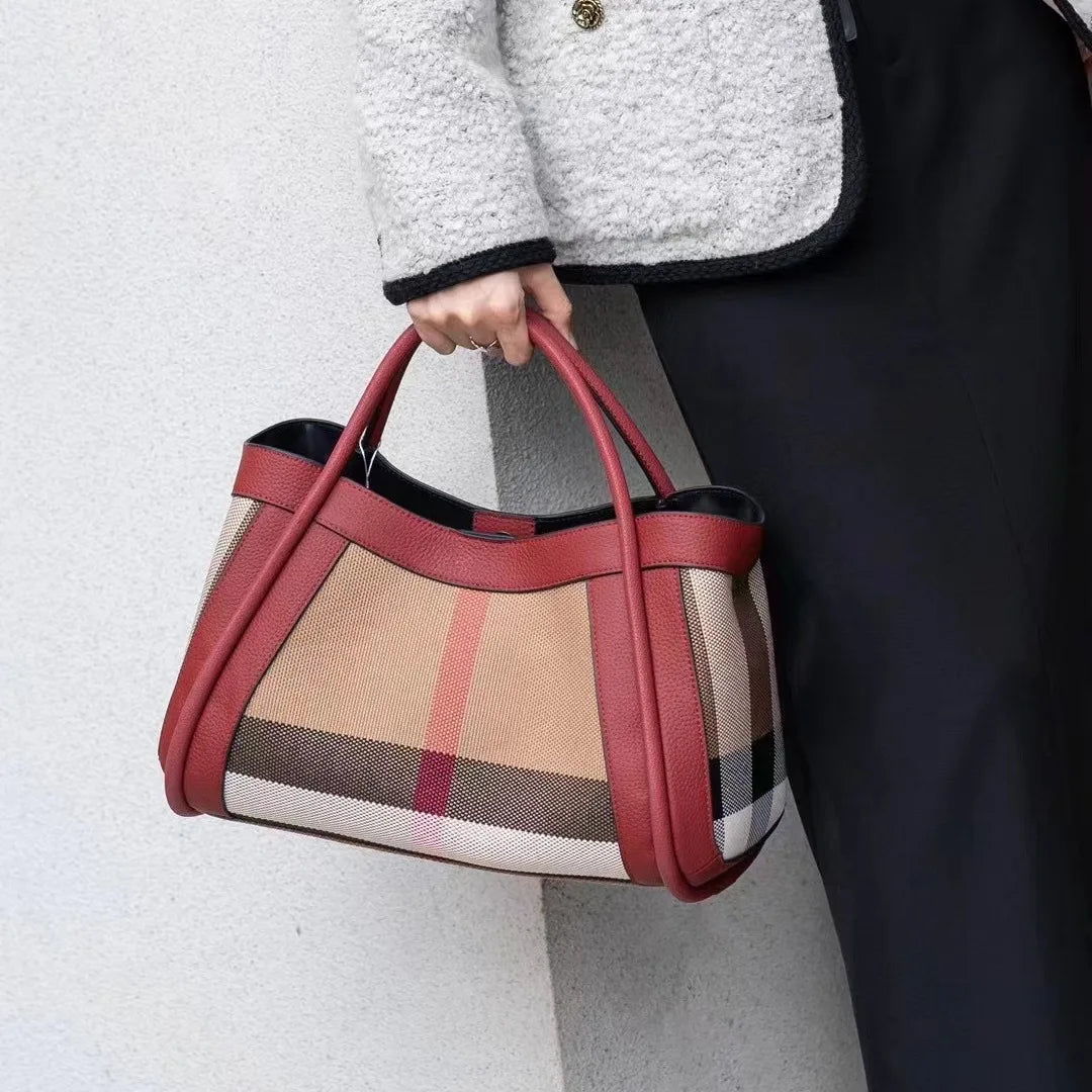 Borsa a mano elegante con motivo a quadri e dettagli in pelle rossa, indossata da una persona con cappotto grigio. Accessorio moda di lusso.