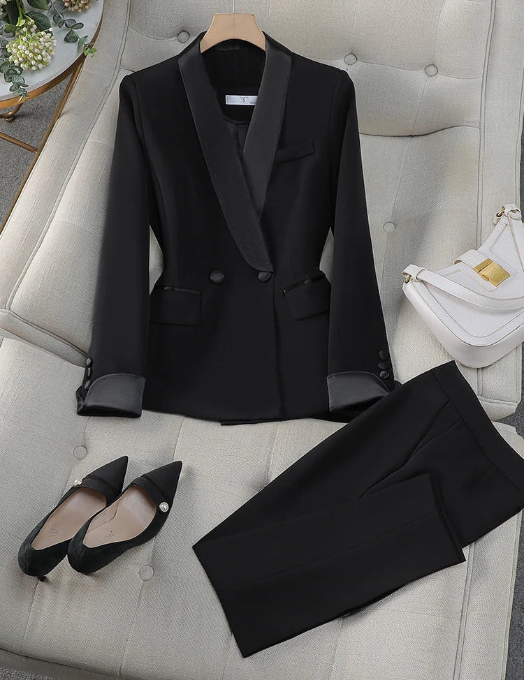 Completo donna elegante nero su divano beige, giacca con revers satinati, pantaloni abbinati, scarpe nere a punta, borsa bianca. Moda formale.