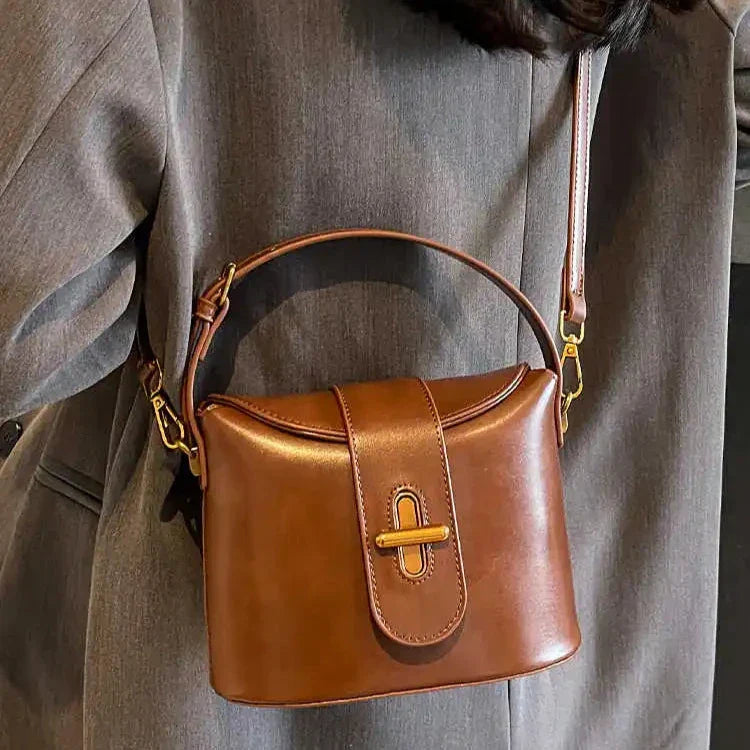Borsa a tracolla in pelle marrone, design elegante, chiusura a patta, indossata su cappotto grigio. Accessorio moda donna, stile casual chic.