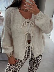 Donna con cardigan beige a maglia grossa con lacci, indossa pantaloni leopardati. Look casual e chic, perfetto per moda autunnale e invernale.