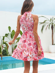 Abito estivo donna rosa floreale, senza maniche, scollo all'americana, sfondo piscina e palme. Moda estiva, abbigliamento casual elegante.
