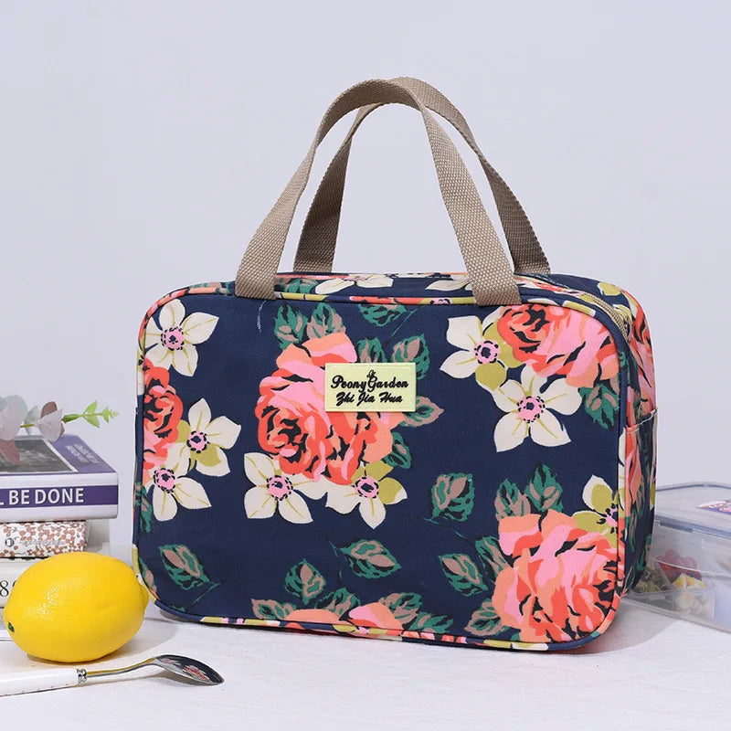 Borsa termica floreale blu con manici beige, ideale per picnic e pranzo al sacco. Design con rose rosa e fiori bianchi. Accessorio pratico e elegante.