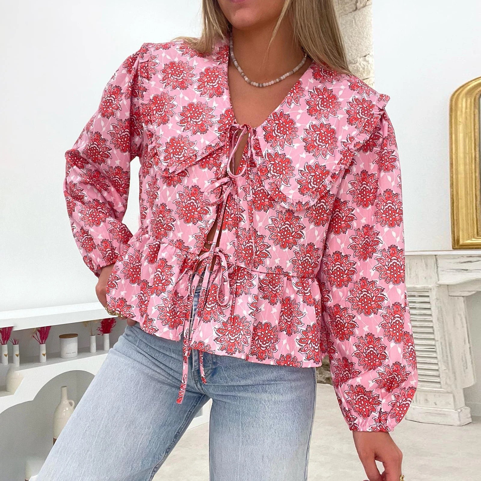 Blusa donna floreale rosa con maniche lunghe e laccetti, abbinata a jeans chiari. Moda casual femminile, stile primaverile, tendenze abbigliamento 2023.