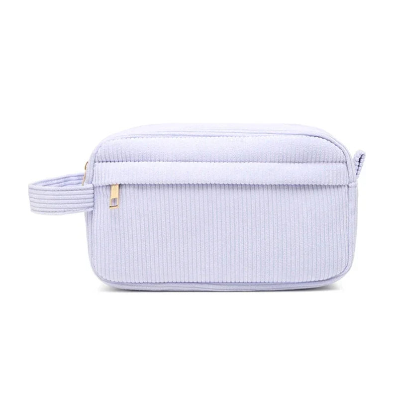 Borsa da toilette in tessuto a coste lilla con cerniera dorata e manico laterale. Elegante e pratica per viaggi e organizzazione bagno.