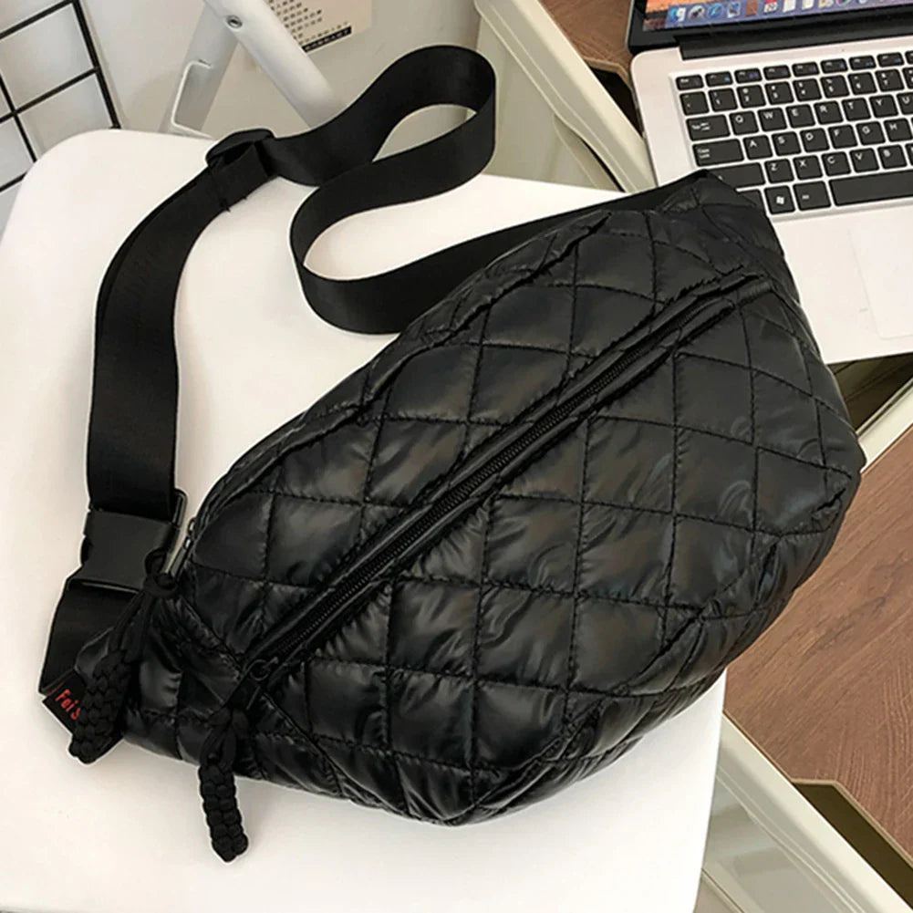 Marsupio nero trapuntato in pelle sintetica, con cerniera e cintura regolabile, su sedia bianca accanto a laptop. Accessorio moda unisex.