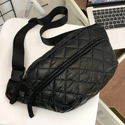 Marsupio nero trapuntato in pelle sintetica, con cerniera e cintura regolabile, su sedia bianca accanto a laptop. Accessorio moda unisex.