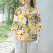 Maglietta donna floreale, maniche corte, colori vivaci, stile casual estivo, indossata con pantaloni bianchi, accessoriata con collana e cappello.