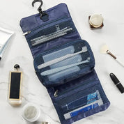 Organizer da viaggio blu aperto su superficie di marmo, con ganci e tasche a rete contenenti spazzolini, dentifricio e accessori da bagno.