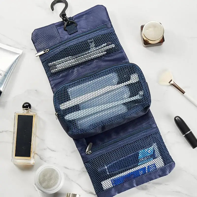 Organizer da viaggio blu aperto su superficie di marmo, con ganci e tasche a rete contenenti spazzolini, dentifricio e accessori da bagno.