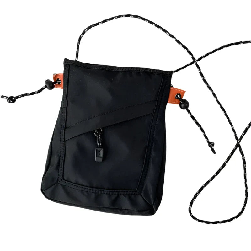Borsa a tracolla nera in nylon con cerniera frontale, dettagli arancioni e cordino regolabile. Accessorio moda unisex, pratico e leggero.
