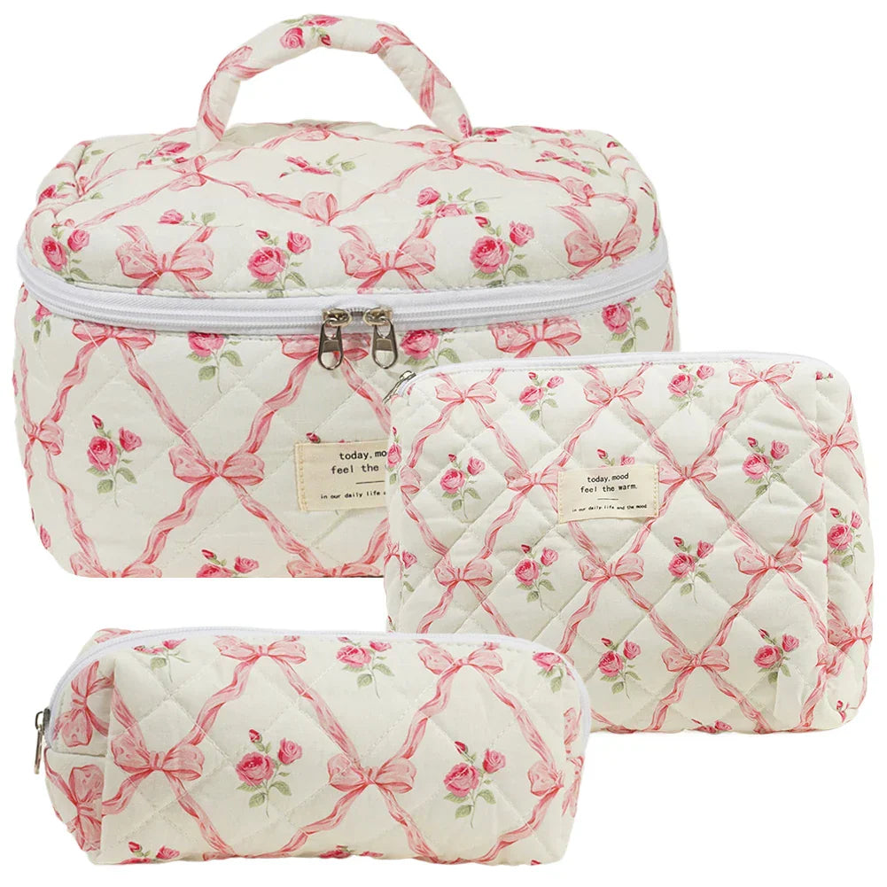 Set di tre beauty case trapuntati bianchi con motivi floreali rosa e fiocchi, chiusura a zip, ideali per viaggi e organizzazione cosmetici.