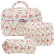 Set di tre beauty case trapuntati bianchi con motivi floreali rosa e fiocchi, chiusura a zip, ideali per viaggi e organizzazione cosmetici.