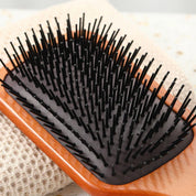 Spazzola per capelli in legno con setole nere su sfondo tessile beige, ideale per districare e lisciare, accessorio essenziale per la cura dei capelli.