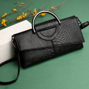 Borsa a tracolla nera in pelle con texture a rettile, manico in metallo, su sfondo verde. Elegante accessorio moda donna.