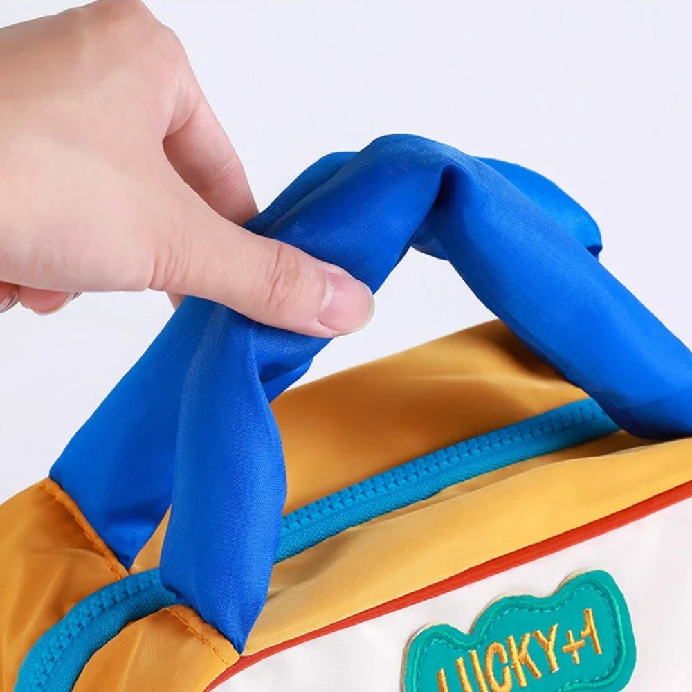 Mano che tiene una borsa termica colorata con manico blu, ideale per picnic e pranzo al sacco. Design moderno, perfetta per conservare cibi freschi.