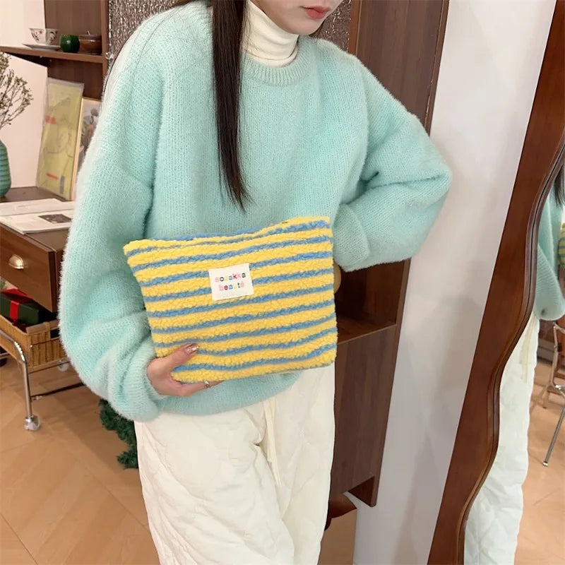 Donna con maglione verde menta tiene borsa a righe gialle e blu. Moda invernale, accessori colorati, stile casual chic.