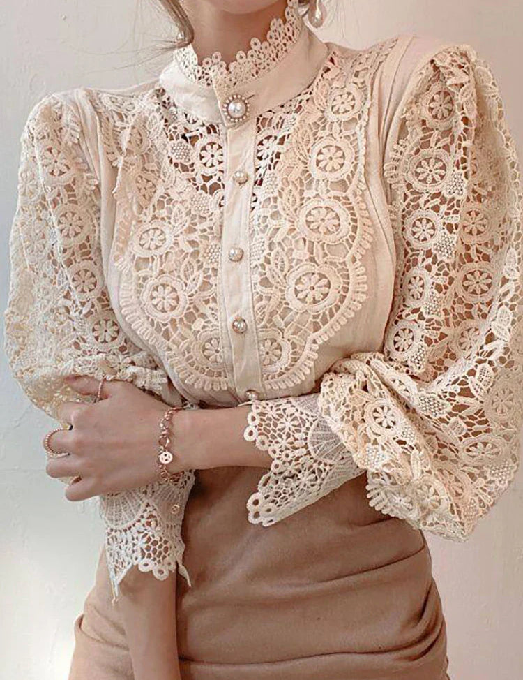 Blusa elegante in pizzo beige con maniche lunghe e dettagli floreali, colletto alto e bottoni decorativi. Moda femminile raffinata e chic.