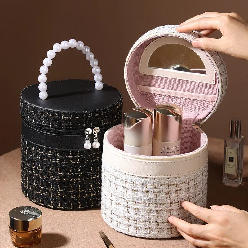 Cofanetto trucco rotondo in tessuto tweed bianco e nero con manico di perle, specchio interno, contenente flaconi cosmetici, su tavolo marrone.