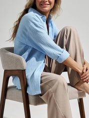 Donna seduta su sedia moderna, indossa camicia azzurra e pantaloni beige. Moda casual elegante, abbigliamento donna, stile rilassato.
