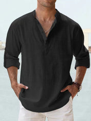 Camicia uomo nera in lino, maniche lunghe arrotolate, colletto alla coreana, abbinata a pantaloni bianchi. Stile casual elegante.