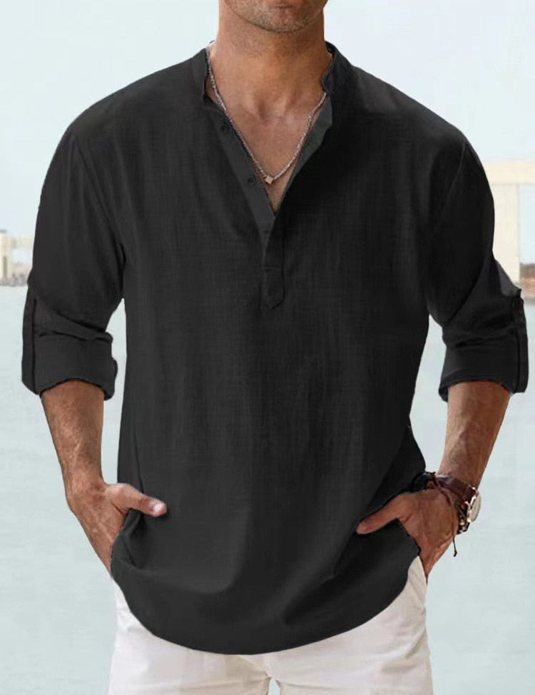 Camicia uomo nera in lino, maniche lunghe arrotolate, colletto alla coreana, abbinata a pantaloni bianchi. Stile casual elegante.