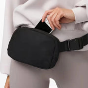 Marsupio nero in tessuto resistente, indossato in vita, con tasca principale aperta e smartphone inserito. Accessorio moda pratico e versatile.