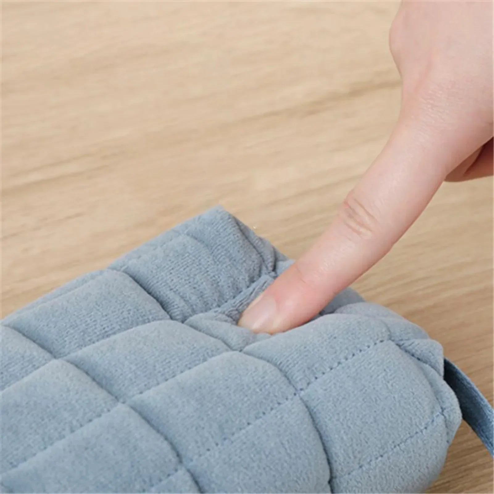 Dito che preme su cuscino grigio trapuntato in tessuto morbido su tavolo di legno. Accessorio casa, comfort, design moderno.