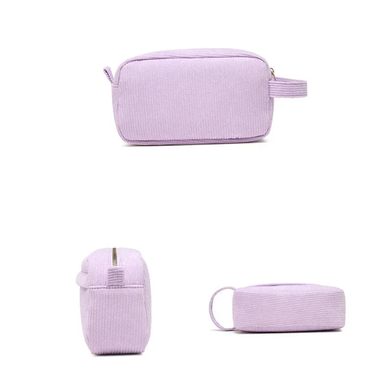 Astuccio da viaggio in velluto a coste lilla, con cerniera dorata e manico laterale. Ideale per cosmetici e accessori. Design elegante e pratico.