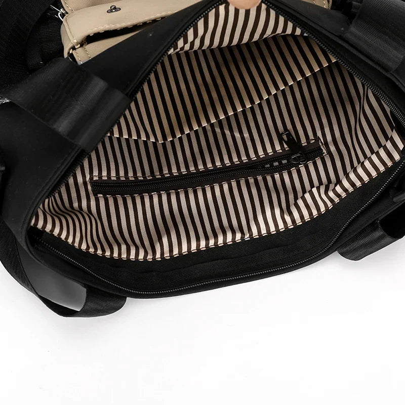 Interno di una borsa nera con fodera a righe bianche e nere, tasca con cerniera. Design elegante, ideale per moda donna e accessori.