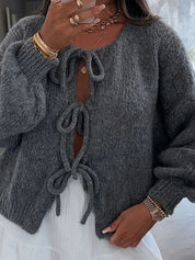 Donna con maglione grigio in lana, dettagli a fiocco, indossa gioielli dorati e orologio. Moda autunnale, stile casual chic.