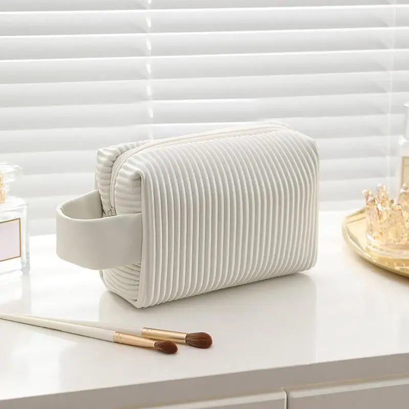Astuccio cosmetico bianco a righe, elegante e moderno, con cerniera e manico laterale. Ideale per trucco e accessori da viaggio.