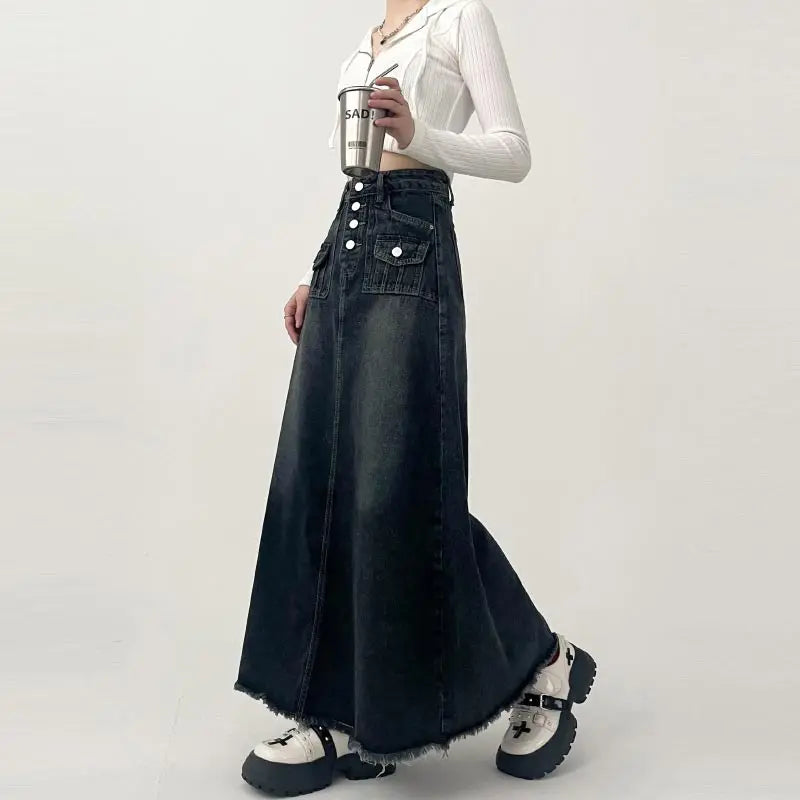 Gonna lunga in denim nero con bottoni, tasche frontali, indossata con camicia bianca e scarpe chunky. Moda casual donna, stile urbano.